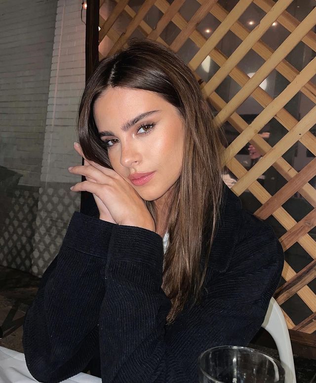 Bridget Satterlee sitting in a cafe posing for her Instagram post wearing a black coat
